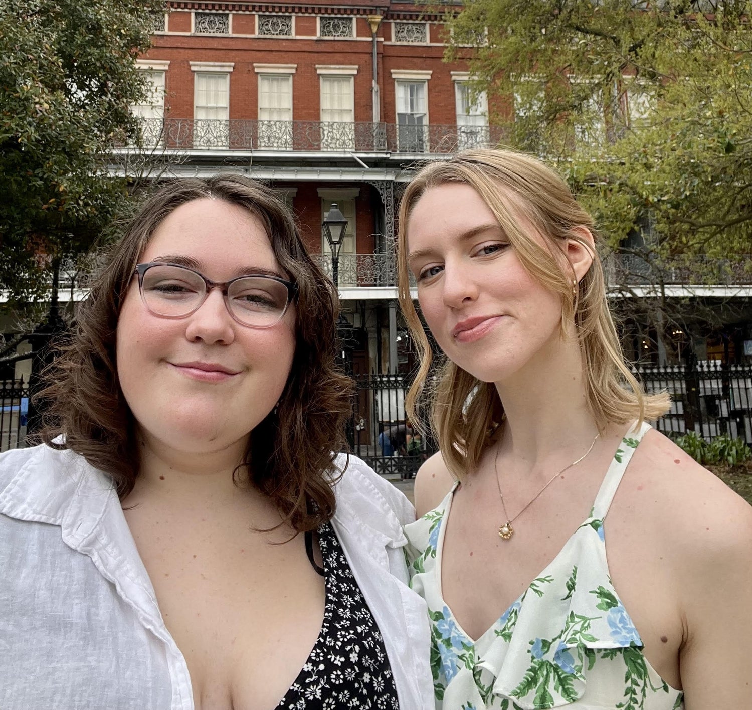 Two young white women in dresses stand side by side smiling. One has dark, curly hair and the other has blond hair pulled back. 